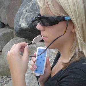 A woman demonstrates the BrainPort V100 vision aid system, in which a video camera positioned between the eyes connects to a processor that feeds electrical pulses to a plate on the tongue. PHOTO COURTESY OF WICAB 